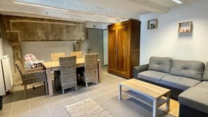 A living room with a grey sofa, a wooden coffee table, wicker chairs, a dining table, and a stone wall. - SIBO GITE apartment 4 pers, swimming pool, nature and city (Boulazac Isle Manoire)