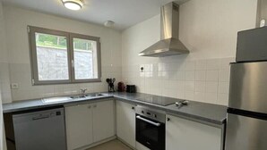 A compact kitchen with white cabinets, a stainless steel refrigerator, a dishwasher, and a window providing natural light. - SIBO GITE apartment 4 pers, swimming pool, nature and city (Boulazac Isle Manoire)