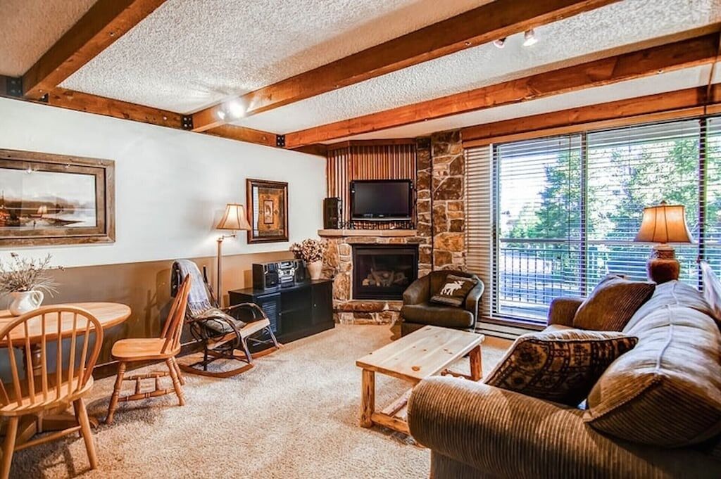 A cozy living room with a stone fireplace, wooden beams, a comfortable sofa, and a television.