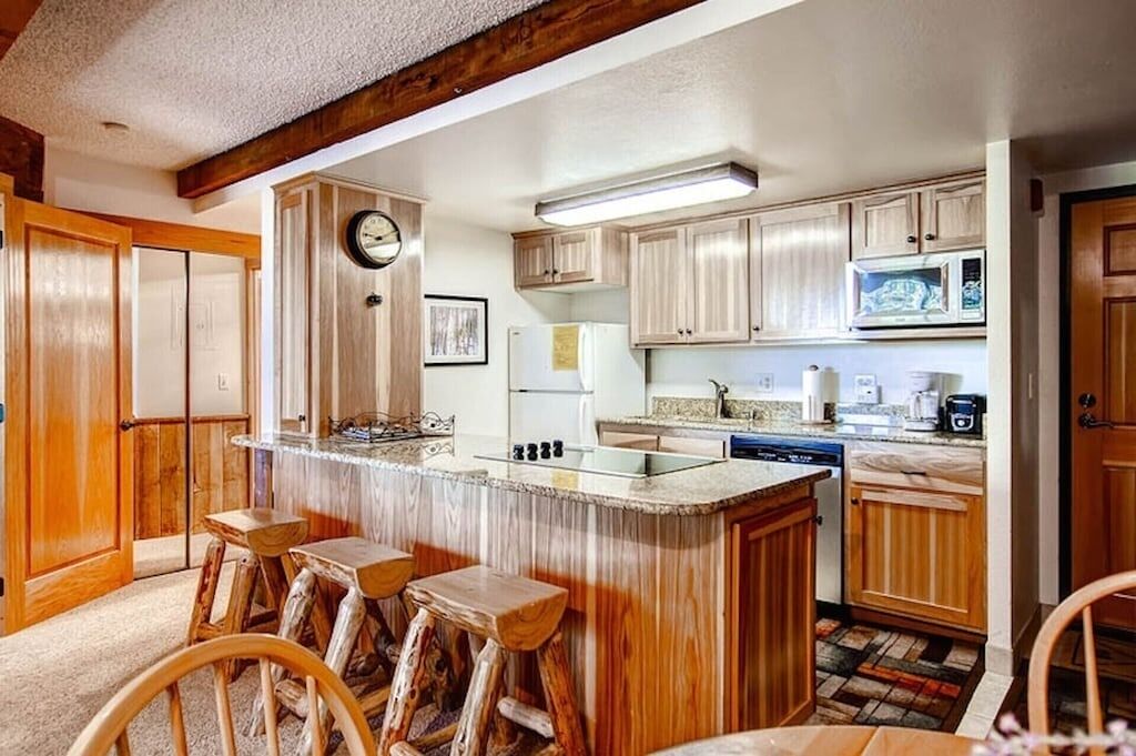 A kitchen with wooden cabinets, a central island with stools, a refrigerator, and a microwave.