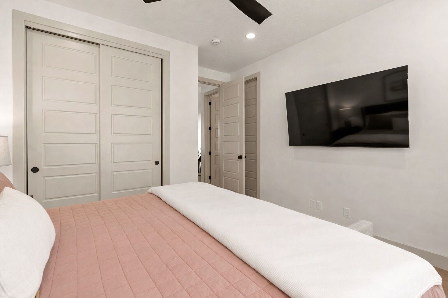 A bedroom with a bed, a TV on the wall, and a closet with sliding doors.