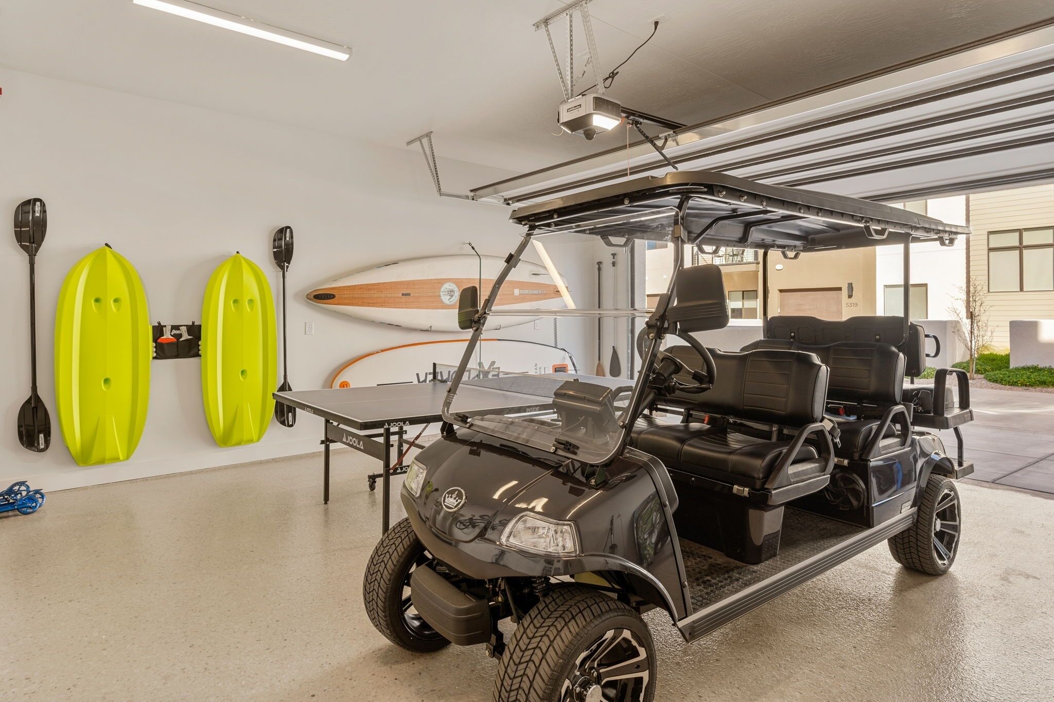 A golf cart in a garage with a surfboard and paddles on the wall.