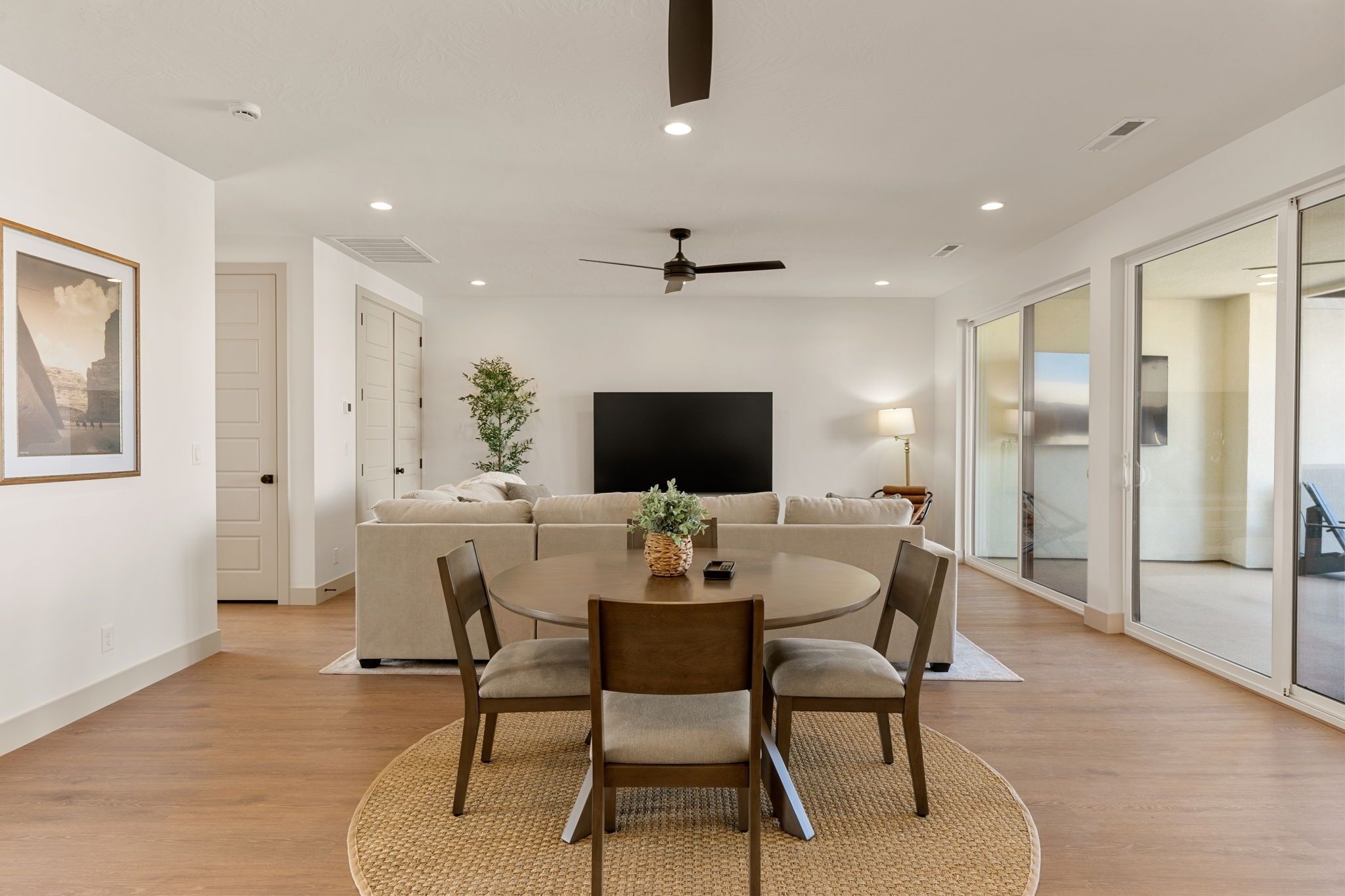 A modern living room with a round dining table, beige sofa, and a flat-screen TV.