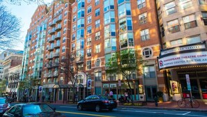 A multi-story building with a theater entrance, a bus stop, and a street with cars and pedestrians. - 2 Bedroom Furnished Apartment near National Museum 2 Apts (Washington)