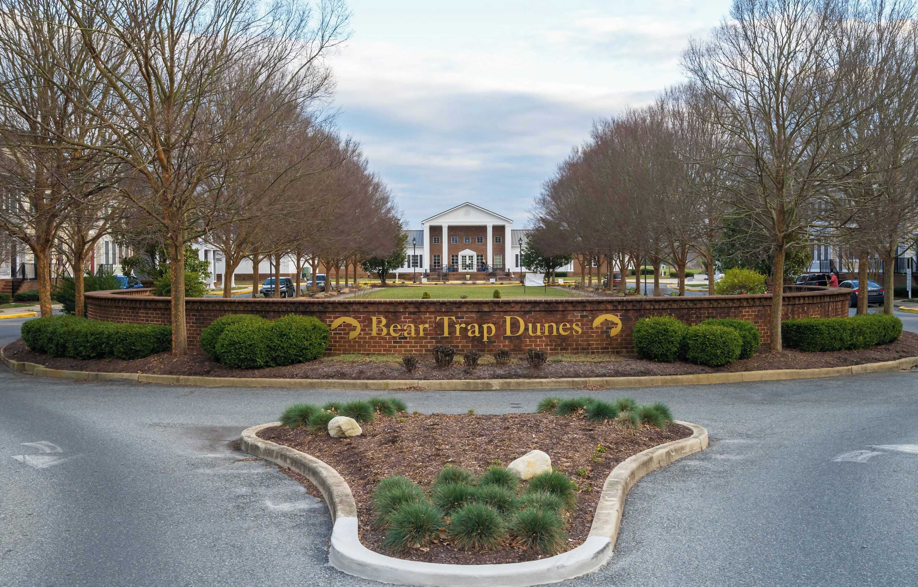 A building with a central entrance flanked by trees and a landscaped area with shrubs and a rock garden.
