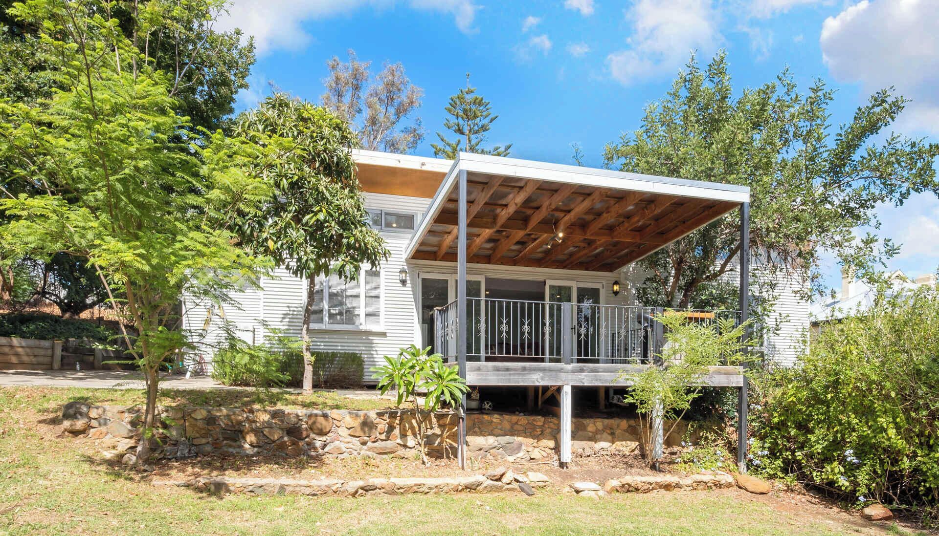 A single-story house with a covered porch, stone retaining wall, and surrounding greenery.
