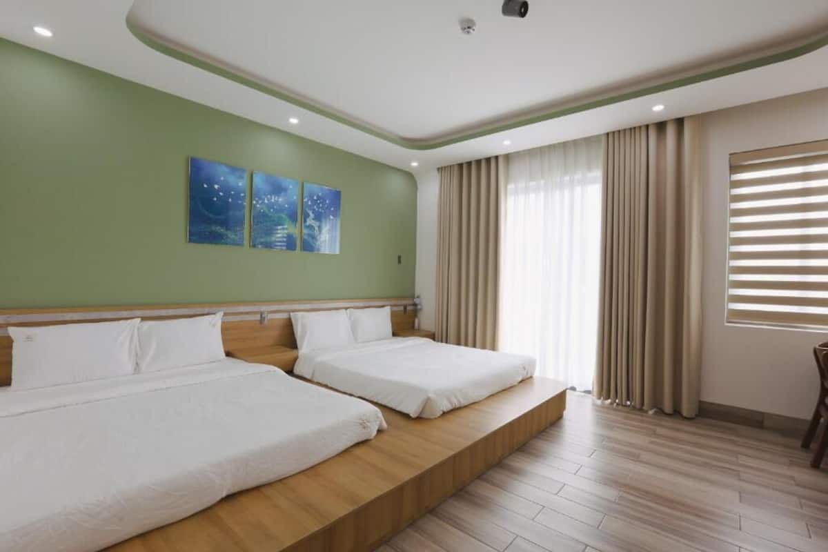 A hotel room with two beds, a green wall, and a large window with curtains.