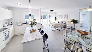 A modern kitchen with white cabinets, a marble countertop, and a dining area with a glass table and chairs. - Puerto Rey - Near the beach with private garden (Vera playa)