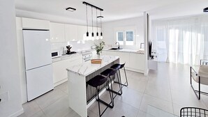 A modern kitchen with white cabinetry, a marble island, and black bar stools. - Puerto Rey - Near the beach with private garden (Vera playa)