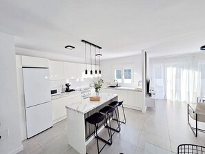 A modern kitchen with white cabinetry, a marble island, and black bar stools. - Puerto Rey - Near the beach with private garden (Vera playa)