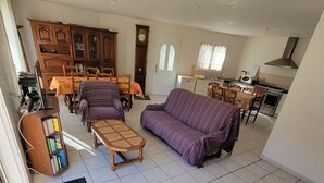 Een ruime woonkamer met een bank, een eettafel en een keuken op de achtergrond.