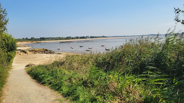 Een rivier met bootjes, een zandstrand en een pad naar het water.