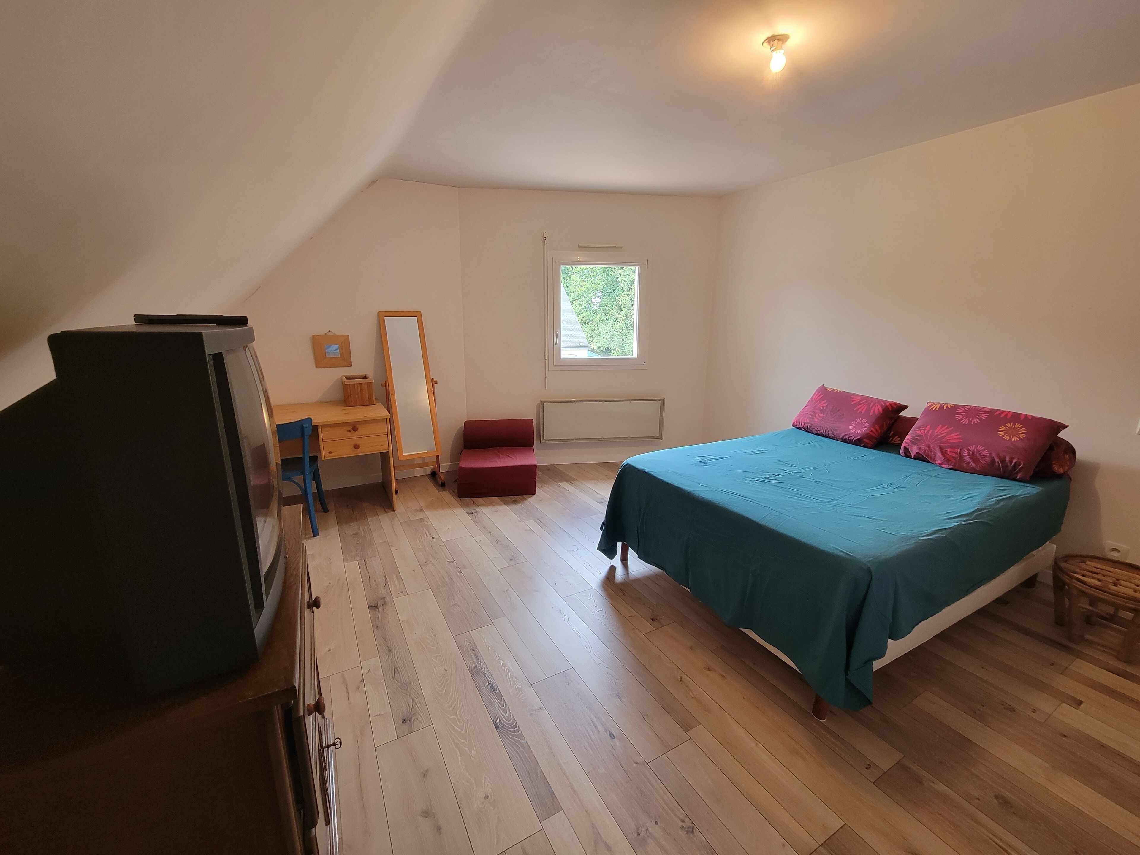 A bedroom with a bed, a desk, a chair, a mirror, and a window.