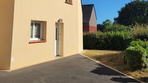 Eenlaags huis met een beige gevel, een donker dak en een kleine voortuin met een verharde oprit.