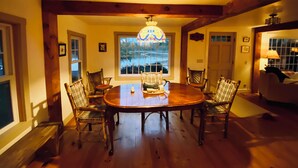 A dining room with a wooden table and chairs, a chandelier, and a view of a lake through a window. - Classic Maine Waterfront Home on the Back River – Trevett (Boothbay)
