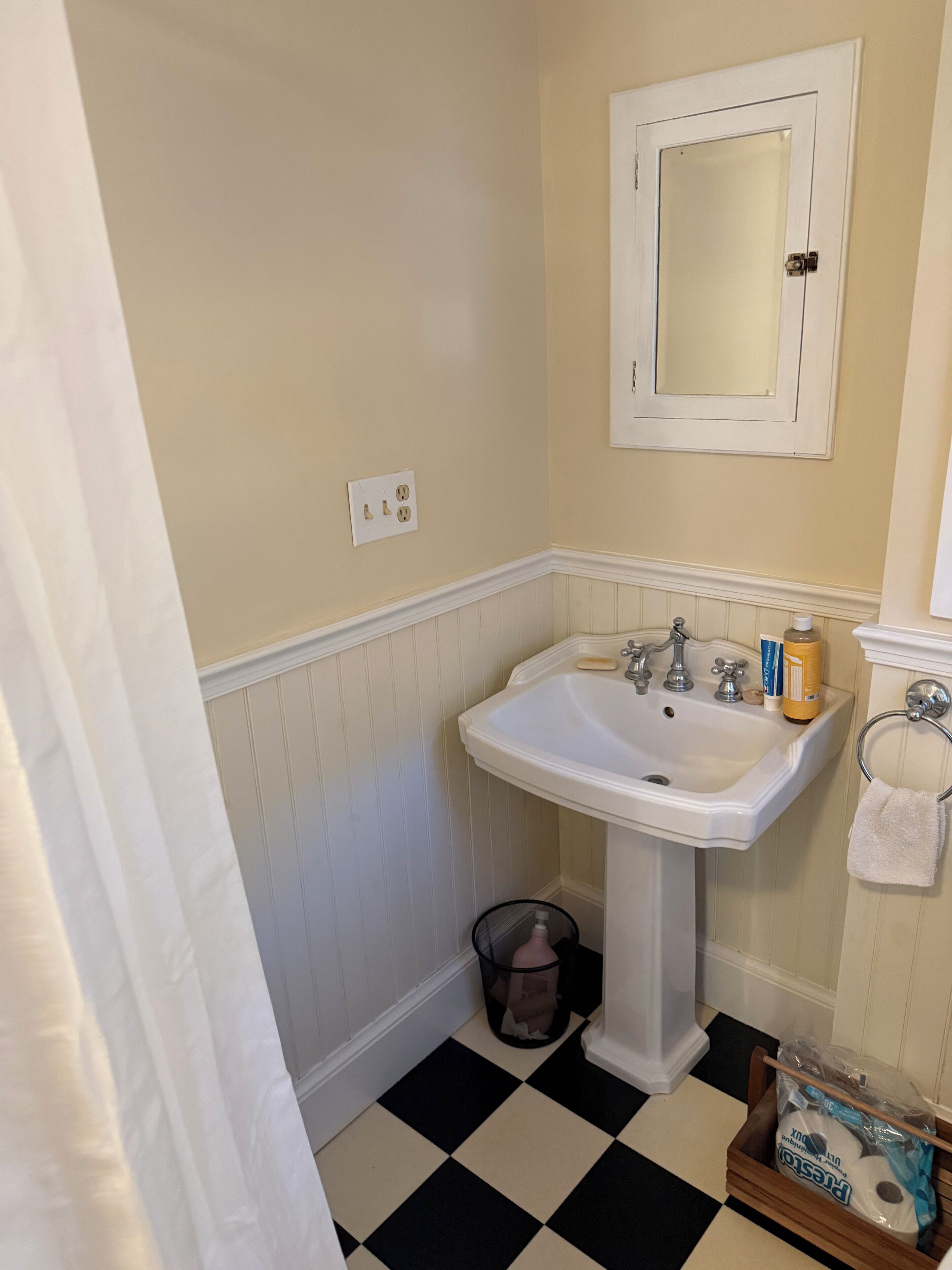 Une salle de bain avec un lavabo blanc, un miroir et un sol à carreaux noirs et blancs.