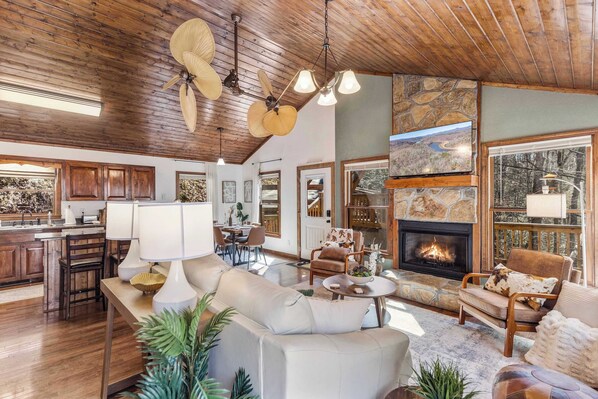 A spacious living area with a fireplace, wooden ceiling, and large windows.