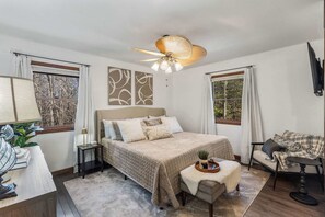 A bedroom with a bed, bedside tables, a desk, a chair, a ceiling fan, and artwork on the walls.