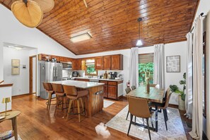 Une cuisine moderne avec des meubles en bois, un îlot central doté de tabourets et un coin repas avec une table et des chaises.