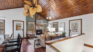 A spacious living area with a wooden ceiling, a fireplace, and a dining area with a bar. - Crooked Lane Cabin - Murphy (Murphy)