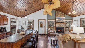A spacious kitchen with a wooden ceiling, a large island with bar stools, and a fireplace in the living area. - Crooked Lane Cabin - Murphy (Murphy)