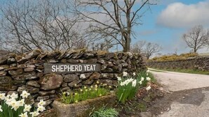 Eine Steinmauer mit einem Schild, das "Shepherd Yeat" zeigt, und Narzissen davor.