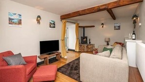 Ein gemütliches Wohnzimmer mit einem roten Sofa, einem beigen Sofa und einem Flachbildfernseher. Ein Kamin mit Holzablage sowie ein kleiner Tisch mit Lampe sind ebenfalls vorhanden.