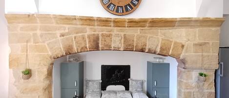 A stone fireplace with a wooden clock above it, a bench with cushions, and two cabinets below.
