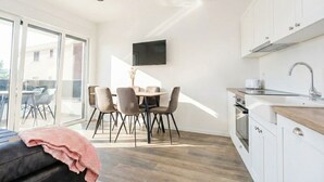 Eine moderne Küche mit weißen Schränken, einem eingebauten Ofen und einer Spüle. Es gibt einen Essbereich mit Tisch und Stühlen sowie einen an der Wand befestigten Fernseher.
