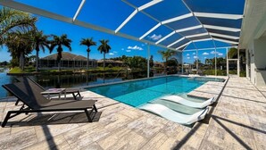 A pool area with lounge chairs, a covered patio, and a clear view of the surrounding landscape. - Villa Elements - new, on water, pool, spa, modern (Cape Coral)