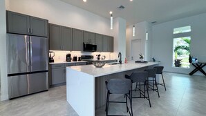 A modern kitchen with a large island, stainless steel appliances, and bar stools. - Villa Elements - new, on water, pool, spa, modern (Cape Coral)