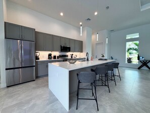 A modern kitchen with a large island, stainless steel appliances, and bar stools. - Villa Elements - new, on water, pool, spa, modern (Cape Coral)