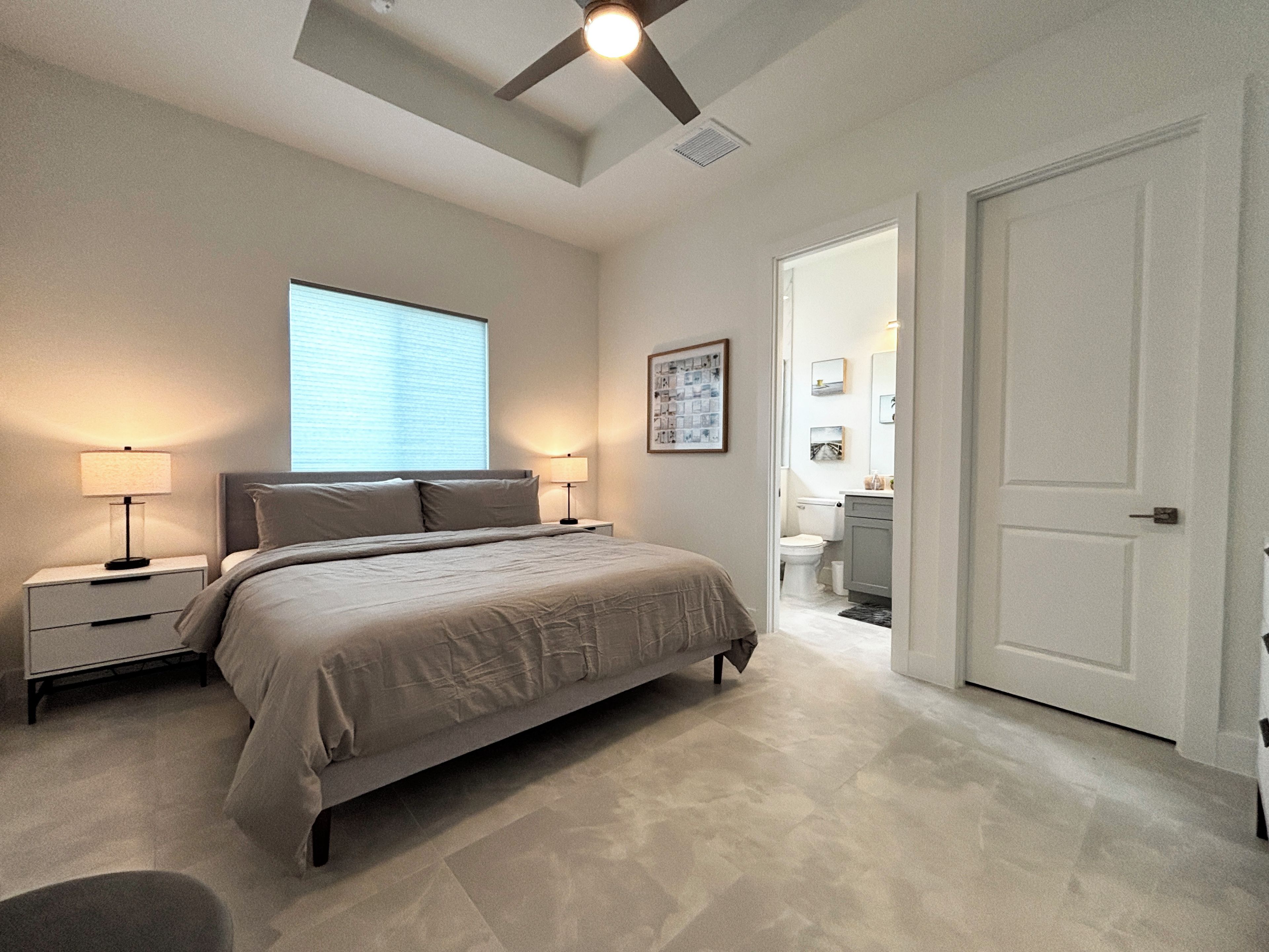Un dormitorio con cama, lámparas de noche, ventilador de techo y ventana.