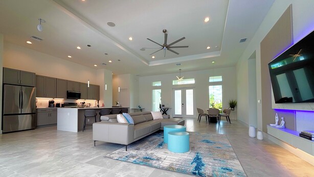 A spacious living area with a large sofa, a coffee table, and a television mounted on the wall. - Villa Elements - new, on water, pool, spa, modern (Cape Coral)