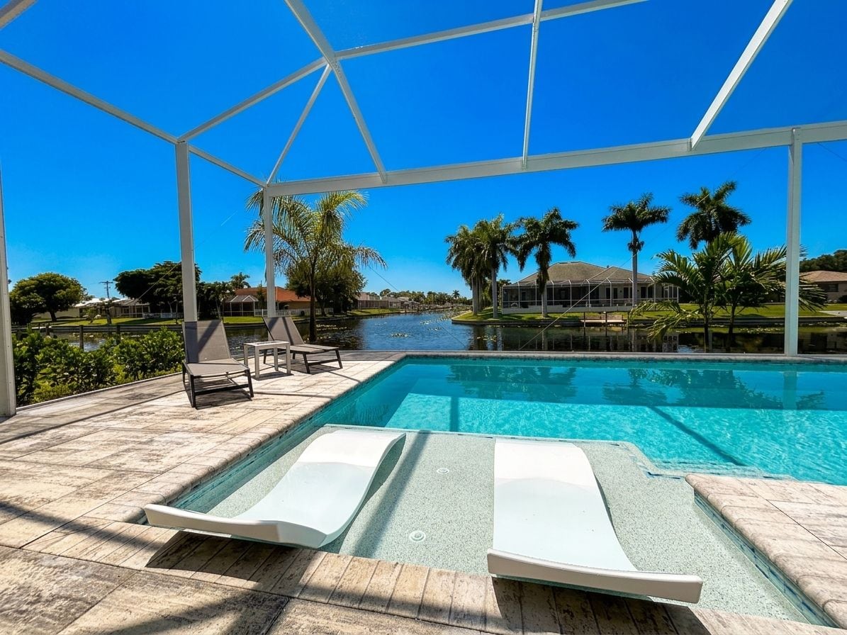 A pool area with lounge chairs, a clear view of a lake, and palm trees in the background.