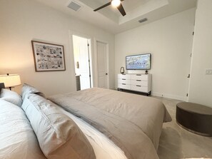 A bedroom with a bed, a dresser, a television, and a ceiling fan. - Villa Elements - new, on water, pool, spa, modern (Cape Coral)
