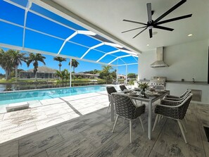 A modern outdoor dining area with a pool, a ceiling fan, and a view of the surrounding landscape. - Villa Elements - new, on water, pool, spa, modern (Cape Coral)