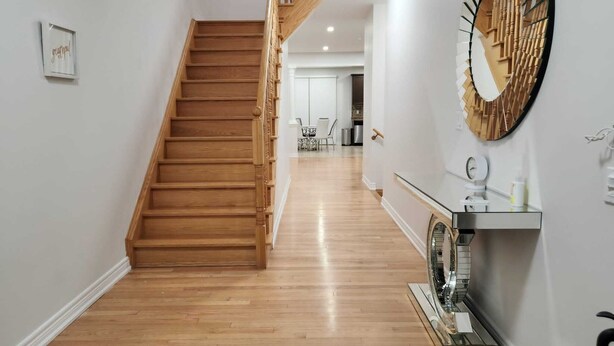 Un escalier menant à un deuxième étage, un couloir avec un miroir et une petite table, et une porte au bout.