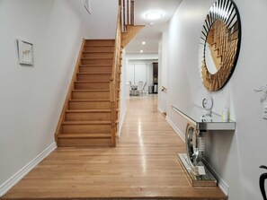 A staircase leading to a second floor, a hallway with a mirror and a small table, and a door at the end.