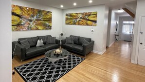 Un salon moderne avec un canapé d’angle, une table basse en verre et deux tableaux abstraits accrochés aux murs.