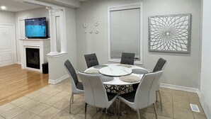Un coin repas comprenant une table ronde, six chaises, une cheminée, un téléviseur et des œuvres d’art décoratives murales.