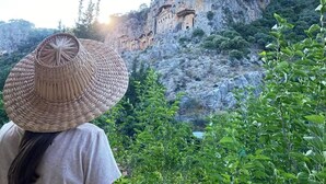 A person with a woven hat overlooking a mountainous area with ancient ruins. - KARYA OTEL (Çandır)