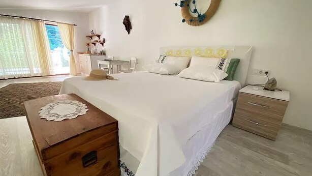 A bedroom with a bed, bedside table, wooden nightstand, and a view of the outdoors. - KARYA OTEL (Çandır)