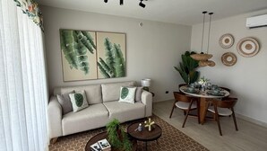 A modern living room with a sofa, coffee table, dining table, and decorative wall art. - Poniente 201 – Tropical Garden Apartment with Pools near Dominicus Beach (Dominicus)