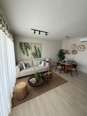 A modern living room with a sofa, coffee table, dining table, and decorative wall art. - Poniente 201 – Tropical Garden Apartment with Pools near Dominicus Beach (Dominicus)