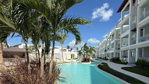 A resort pool with clear water, surrounded by palm trees and modern buildings. - Poniente 201 – Tropical Garden Apartment with Pools near Dominicus Beach (Dominicus)