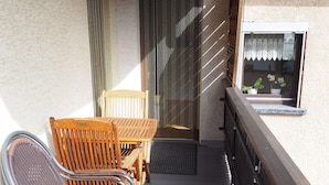 A wooden deck with a table and chairs, a window with lace curtains, and a wall-mounted security camera. - Vacation apartment Haus Junk am Lieserpfad (Daun)