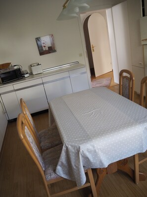 A small, clean kitchen with white cabinets, a microwave, a toaster, and a small refrigerator. There is a dining table with a polka dot tablecloth and two wooden chairs. - Vacation apartment Haus Junk am Lieserpfad (Daun)