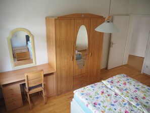 A bedroom with a wooden wardrobe, a desk with a chair, a bed with a floral bedspread, and a mirror on the wall. - Vacation apartment Haus Junk am Lieserpfad (Daun)