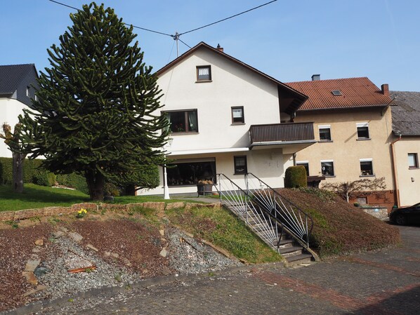 A two-story house with a balcony, a staircase, and a large tree in the yard. - Vacation apartment Haus Junk am Lieserpfad (Daun)